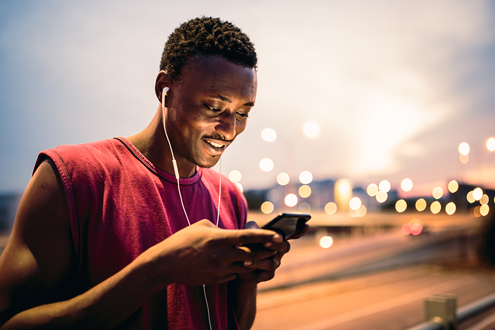 年轻的非洲男子训练后在户外休息，在城市环境中，使用手机
