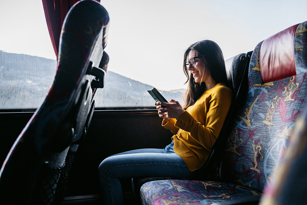 年轻美丽的白人女子在乘公共汽车旅行时阅读新闻或使用智能手机查看社交媒体。