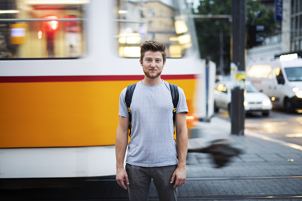 男性肖像在电车周围的城市街道,他站在面前模糊运动电车和车辆在背景和注视镜头。