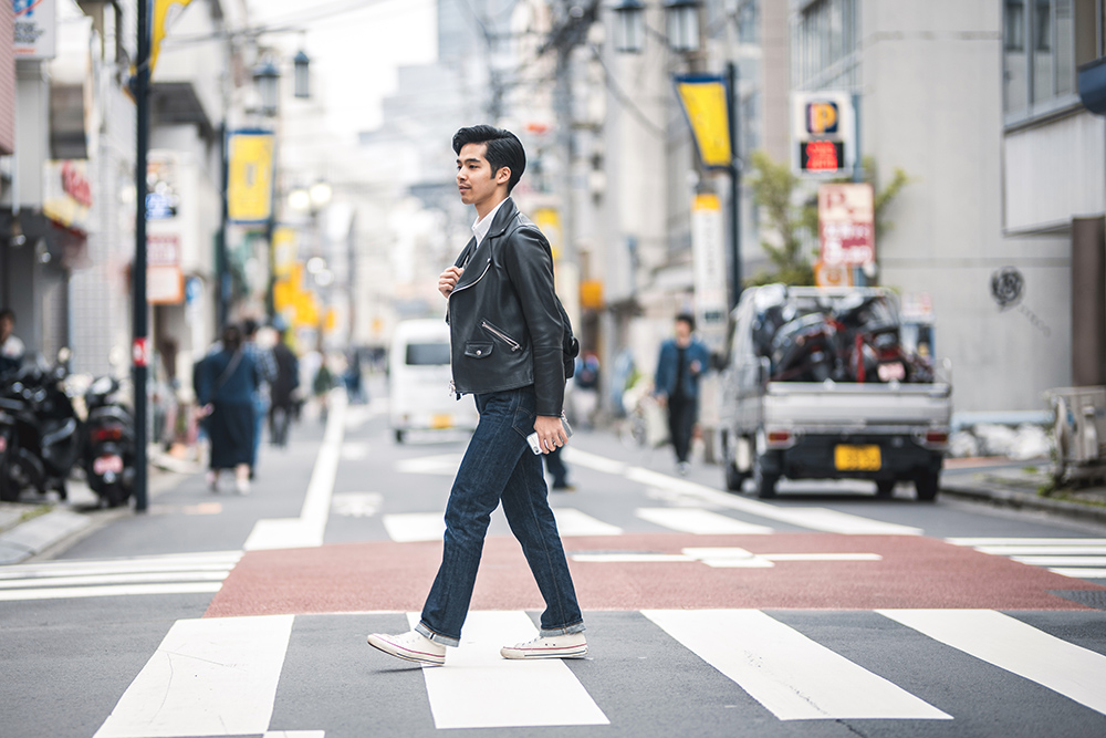 年轻的日本男子大步走过人行斑马线上休息放松的城市在城市东京。